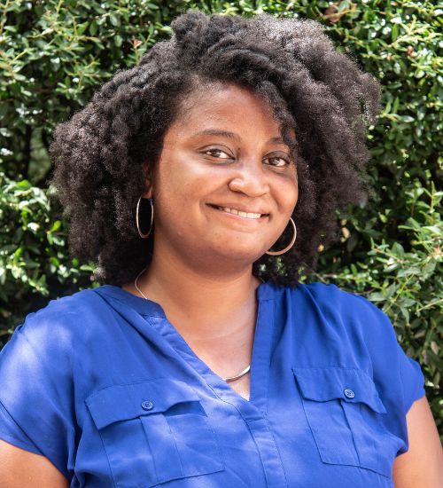 Dr. Jenee Duncan smiles in front of a tree. She is wearing a blue blouse.