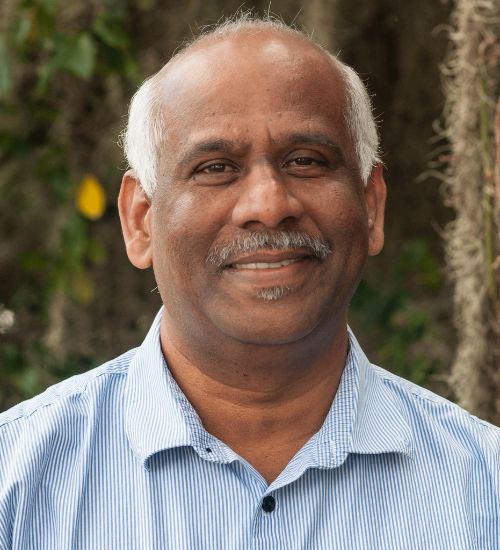Dr. Muthusami Kumaran smiles in front of a tree.