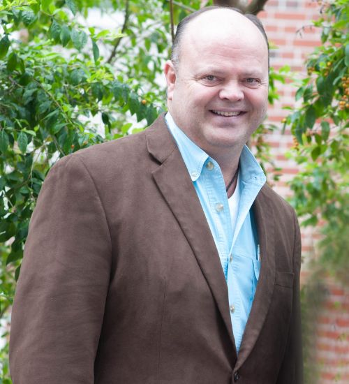 Dr. Randy Cantrell smiles in front of a university building. He is wearing a brown suit.